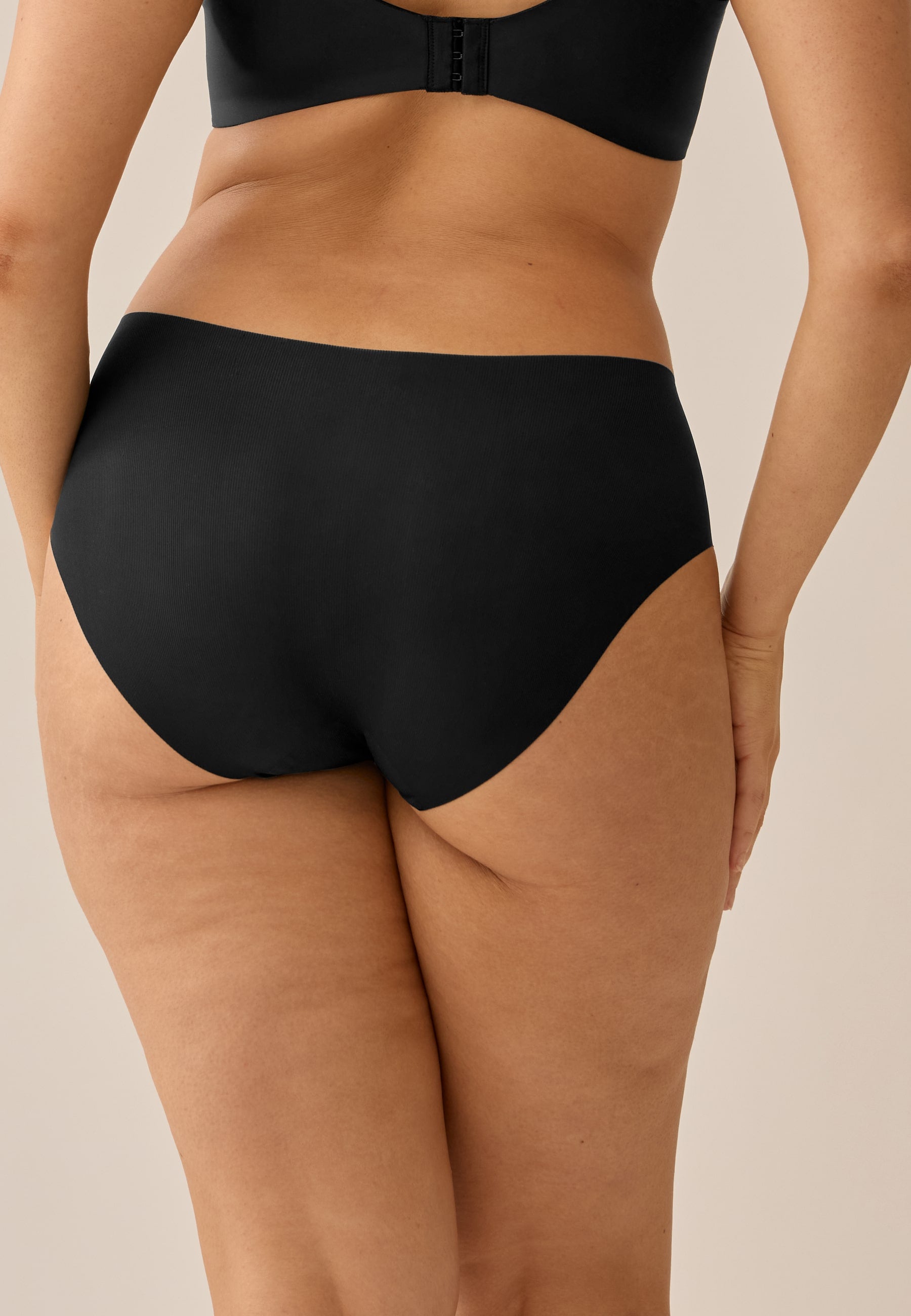 Model trägt NATURANA Everyday Slip und BH in der Farbe schwarz, stehend in Rückenansicht/Nahaufnahme