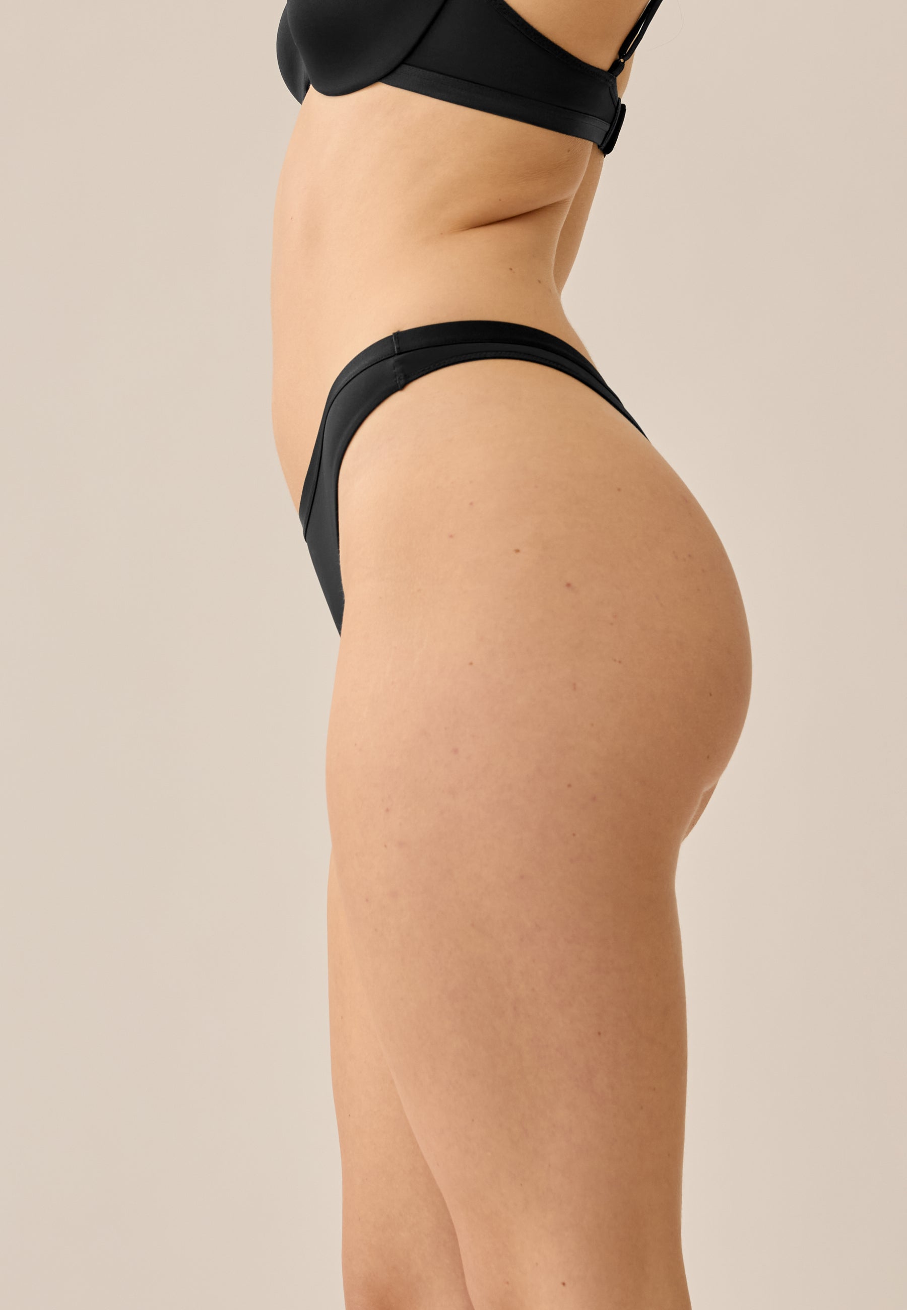 Model steht im Seitenprofil in NATURANA BH mit Bügel und String in der Farbe schwarz