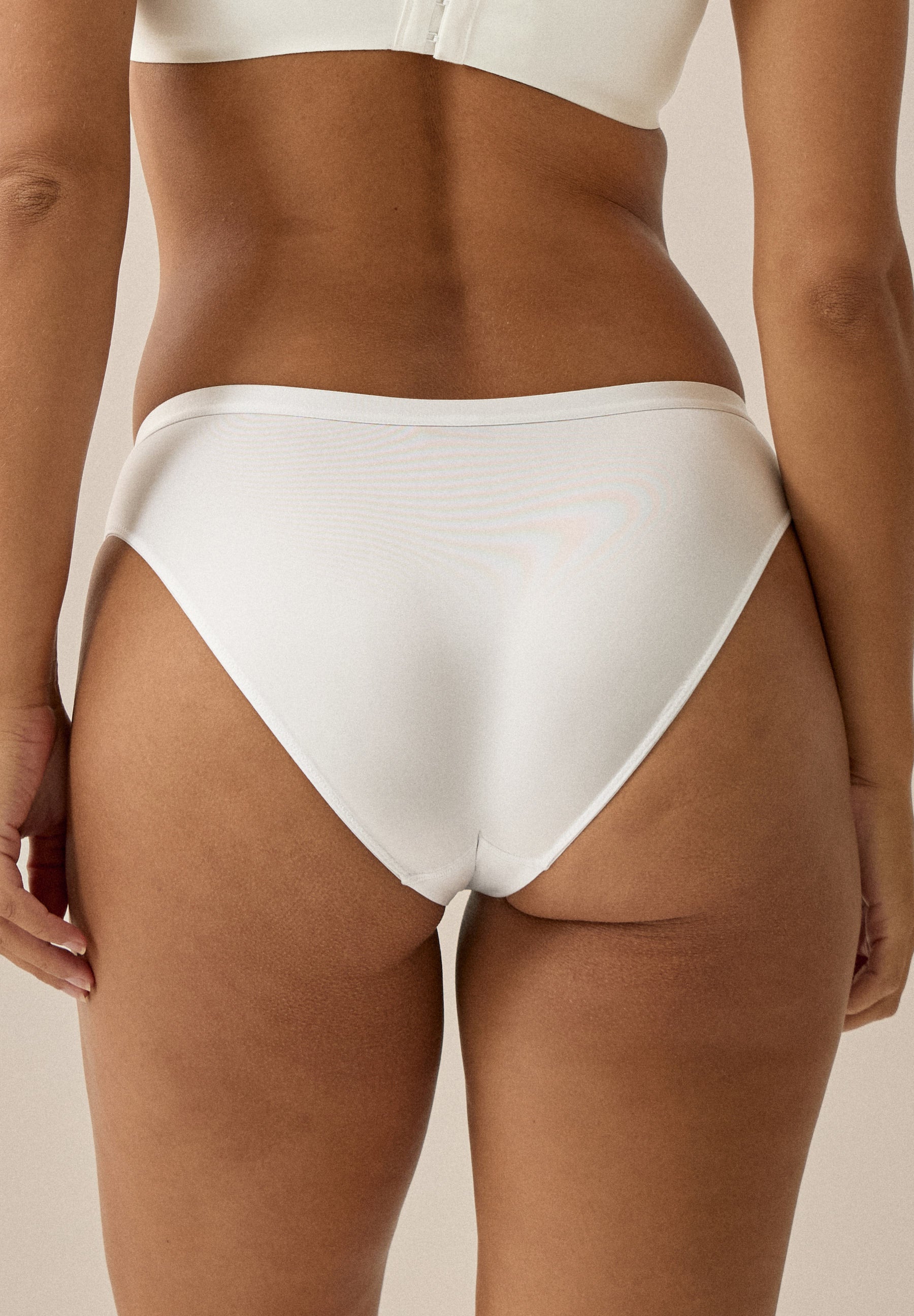 Rückansicht einer Frau in weißem NATURANA Slip; sichtbar sind Rücken, Hüfte bis zum Oberschenkel.