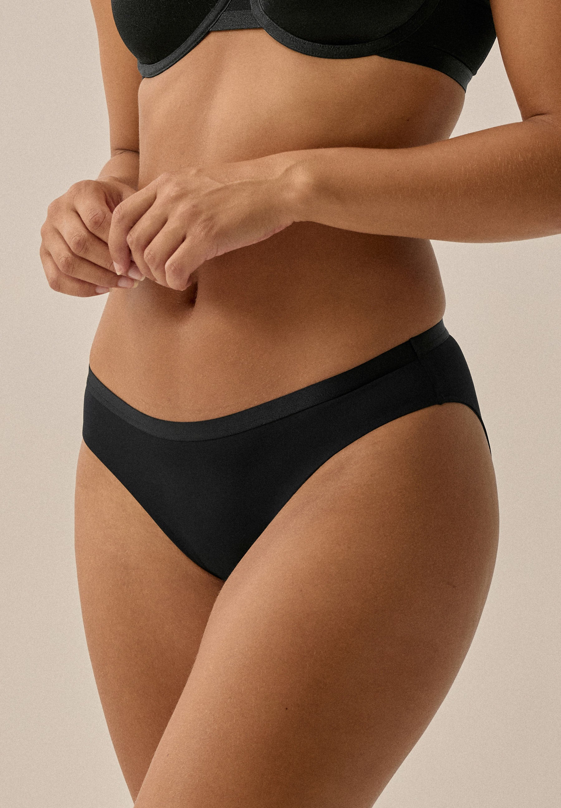 Frontansicht einer Frau in schwarzem NATURANA Slip; sichtbar sind Bauch, Hüfte und Gesäß bis zu den Oberschenkeln.
