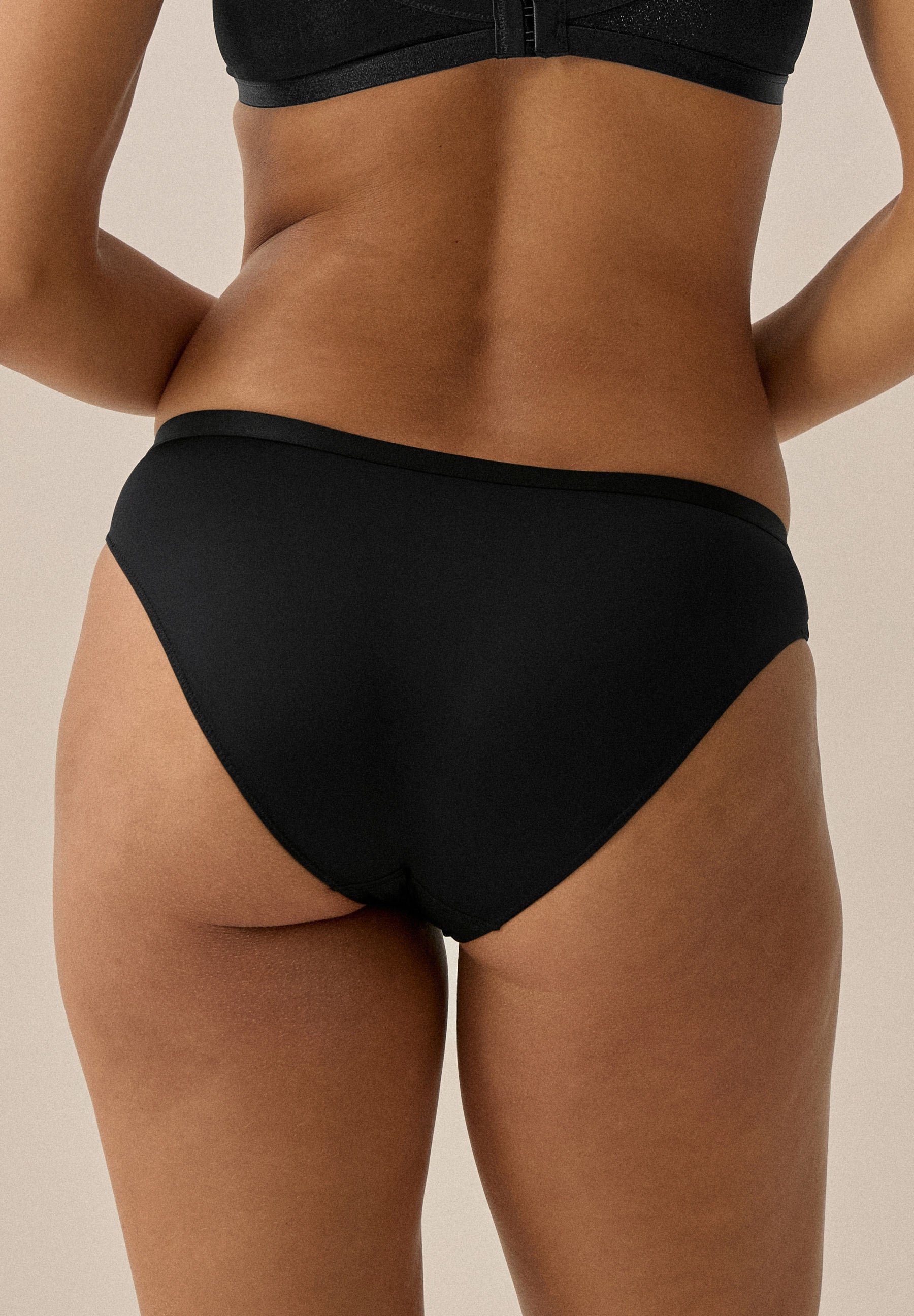 Rückansicht einer Frau in schwarzem NATURANA Slip; sichtbar sind Rücken, Hüfte und Gesäß bis zu den Oberschenkeln.