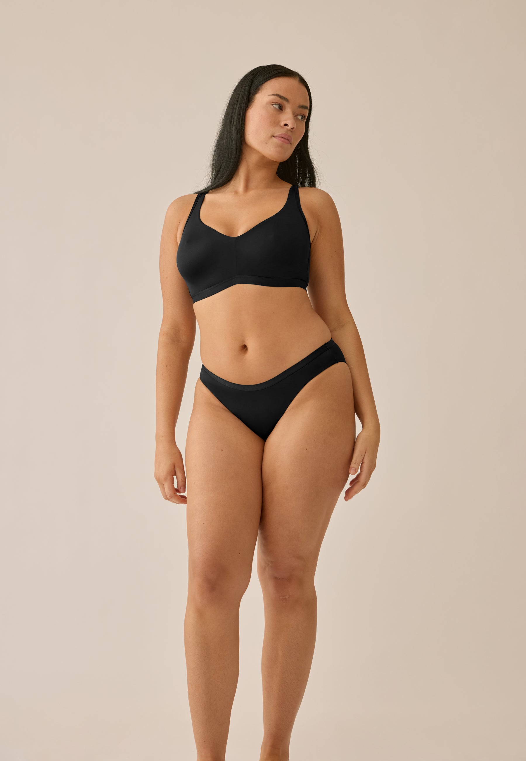 Model posiert stehend in NATURANA BH ohne Bügel und Slip in der Farbe schwarz