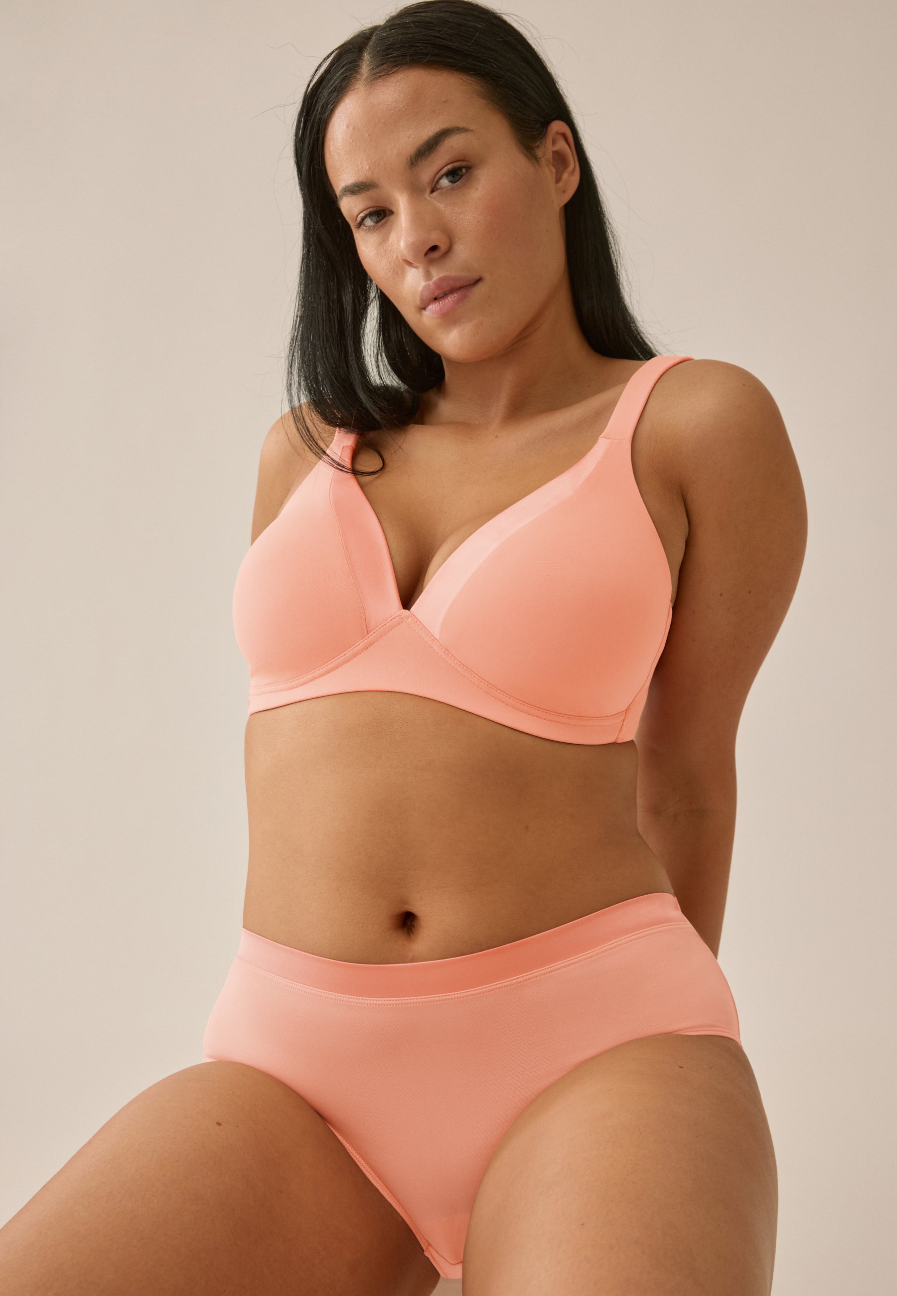 Model posiert sitzend in Frontansicht in NATURANA Schalen-BH ohne Bügel und Panty in der Farbe Clay