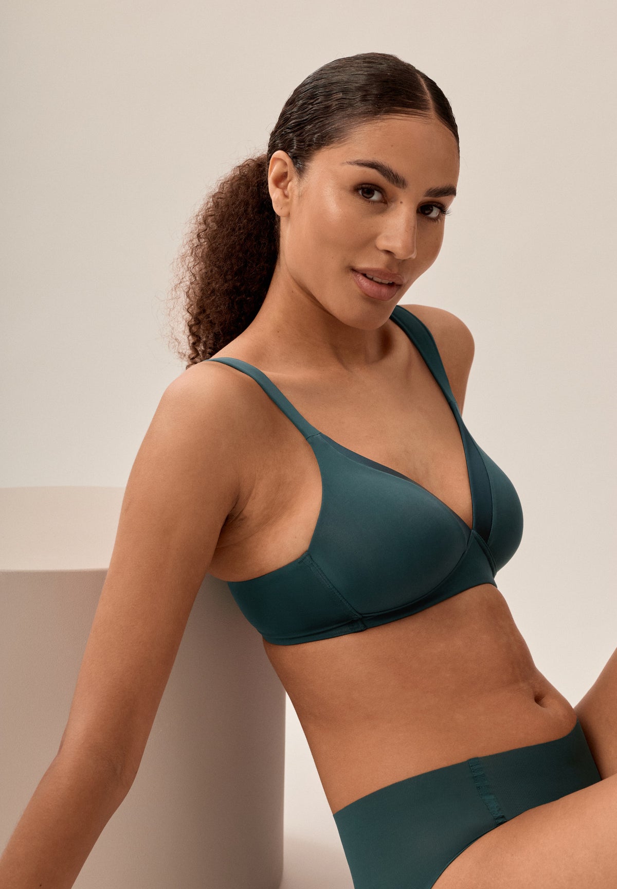 Tannengrüner bügelloser NATURANA Schalen-BH mit breiten Trägern und passender Panty, sitzendes Model leicht seitlich