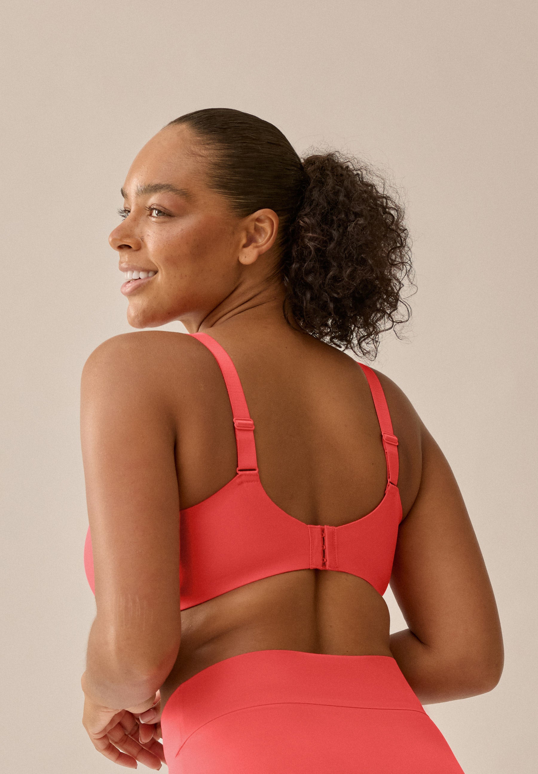 Das Model trägt den Sidesmoother-BH und -Slip von Naturana in der Farbe Chayenne Red mit einem Blickwinkel von hinten