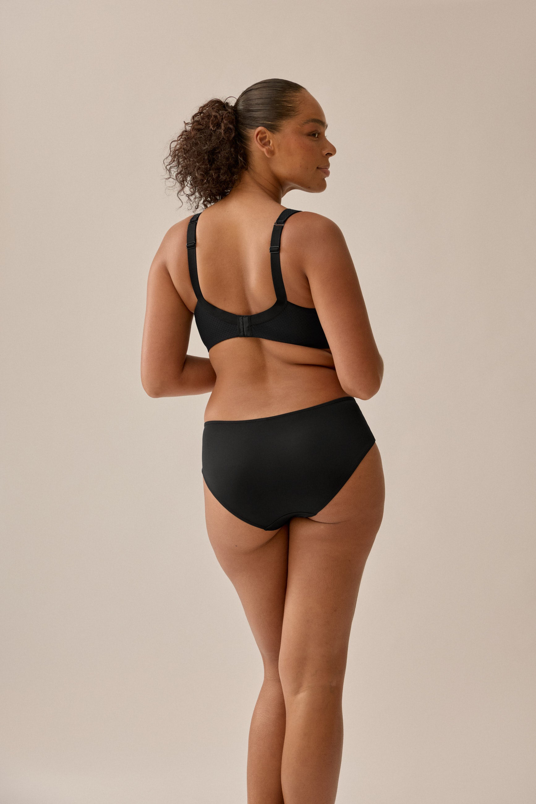 Foto des Models, das das schwarze BH- und Slip-Set von Naturana mit Jacquard-Muster trägt, mit einem Winkel von hinten