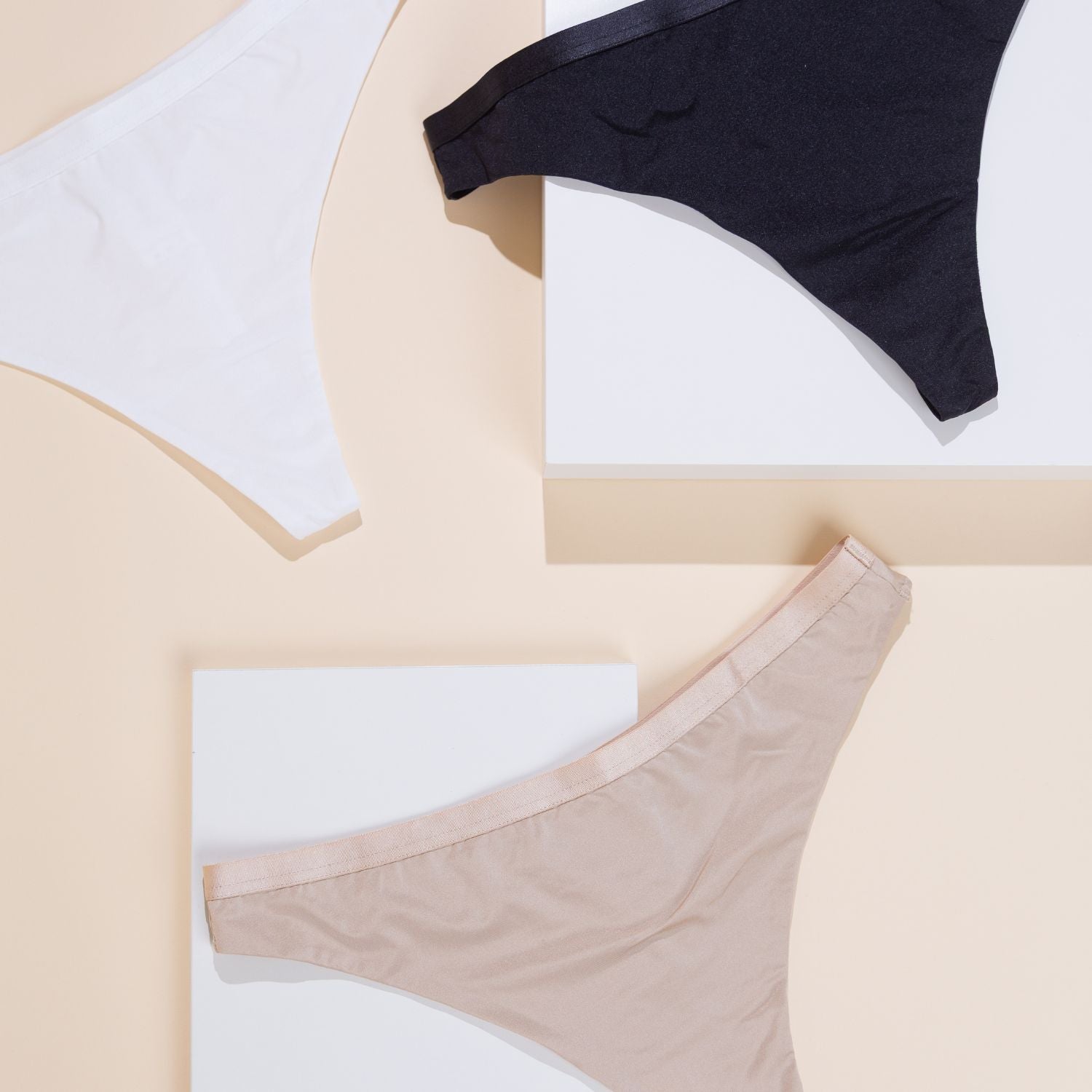 Foto mit den 3 neuen Friday x Lace String-Slips aus der Thursday-Kollektion, in Weiß, Schwarz und Hellbeige auf weißem und beigem Hintergrund