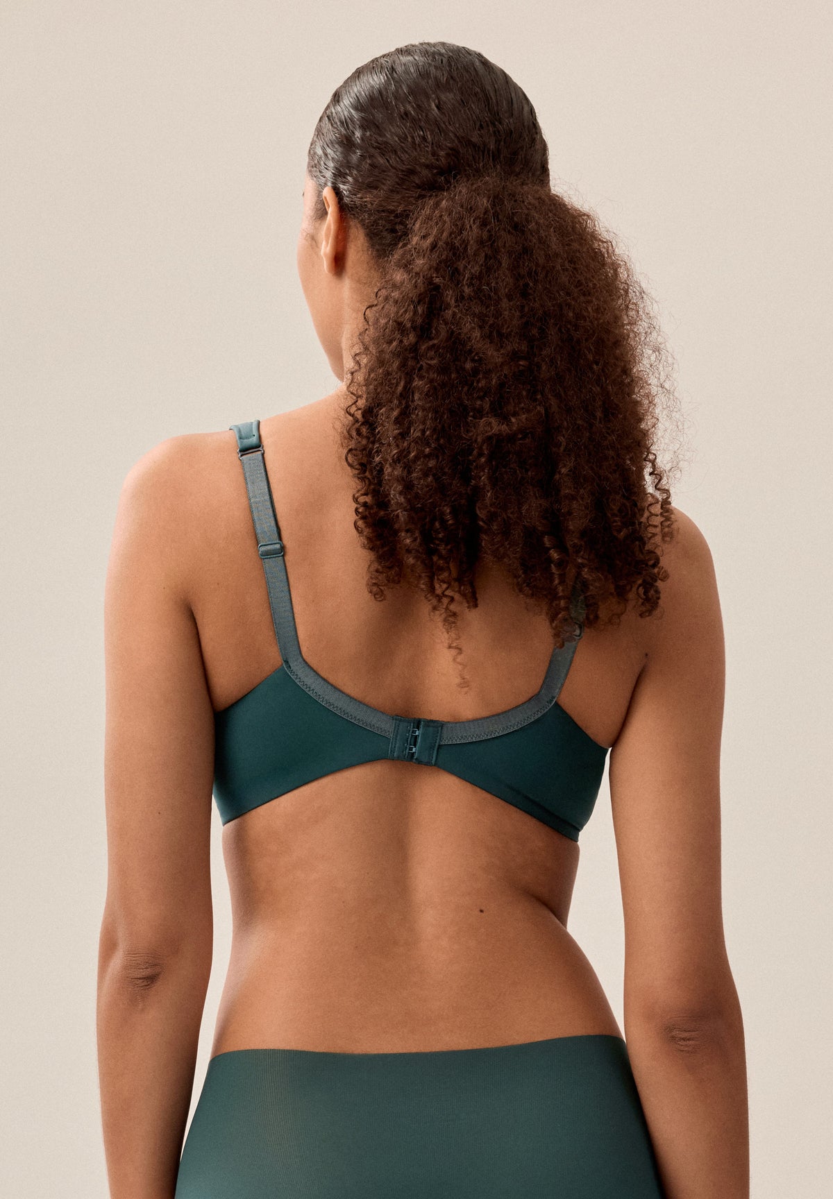 Tannengrüner bügelloser NATURANA Schalen-BH mit breiten Trägern und passender Panty, stehendes Model von hinten