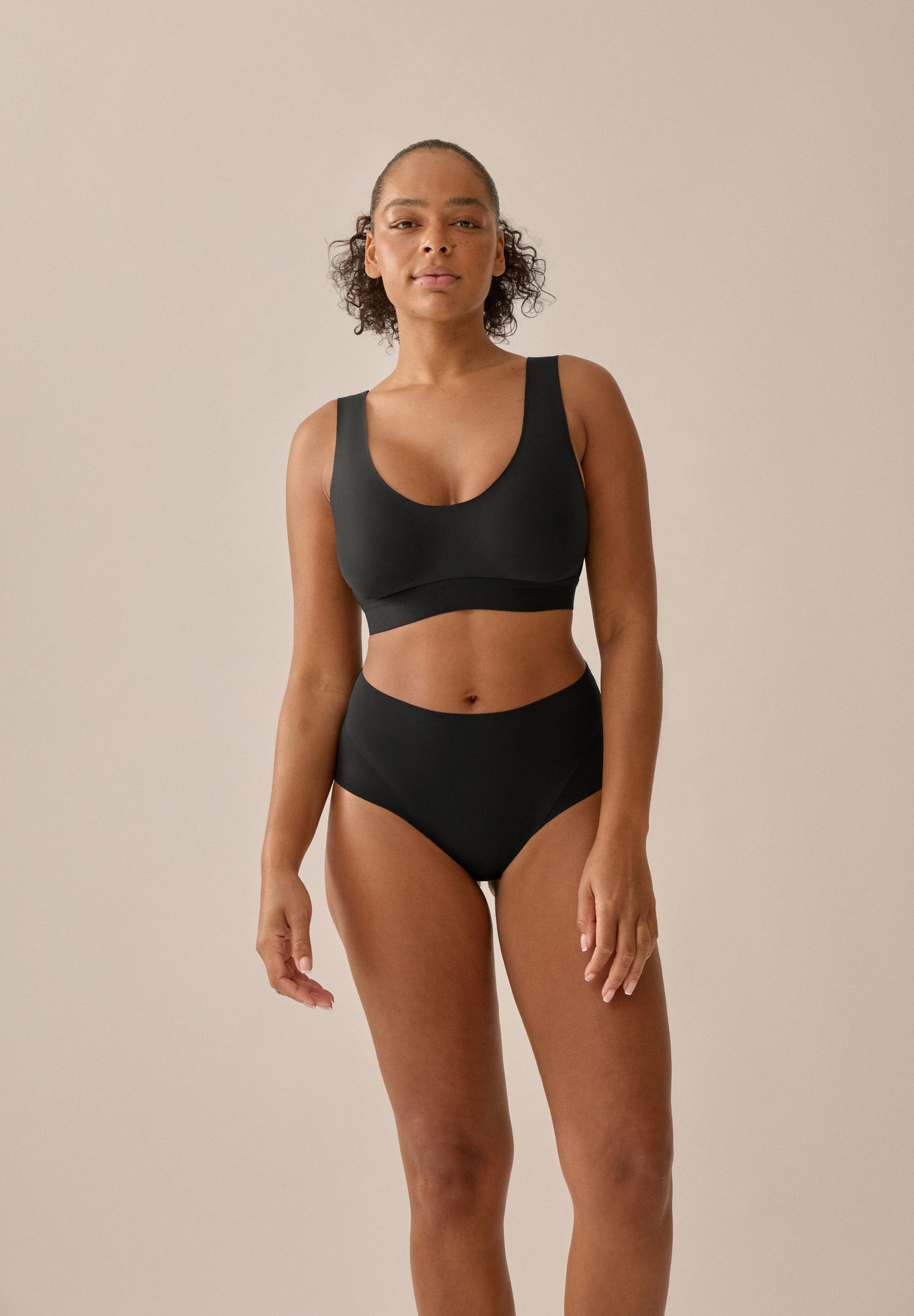 Model mit schwarzem BH und Slip aus der neuen glättenden BH-Kollektion von Naturana, mit weitem Blickwinkel von vorne